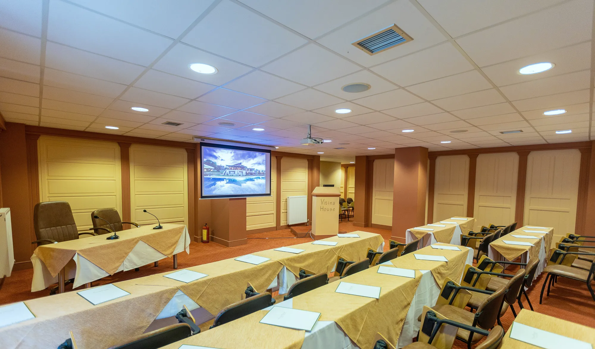 The conference room set with long tables in rows, each with notepads, facing a projection screen and a lectern