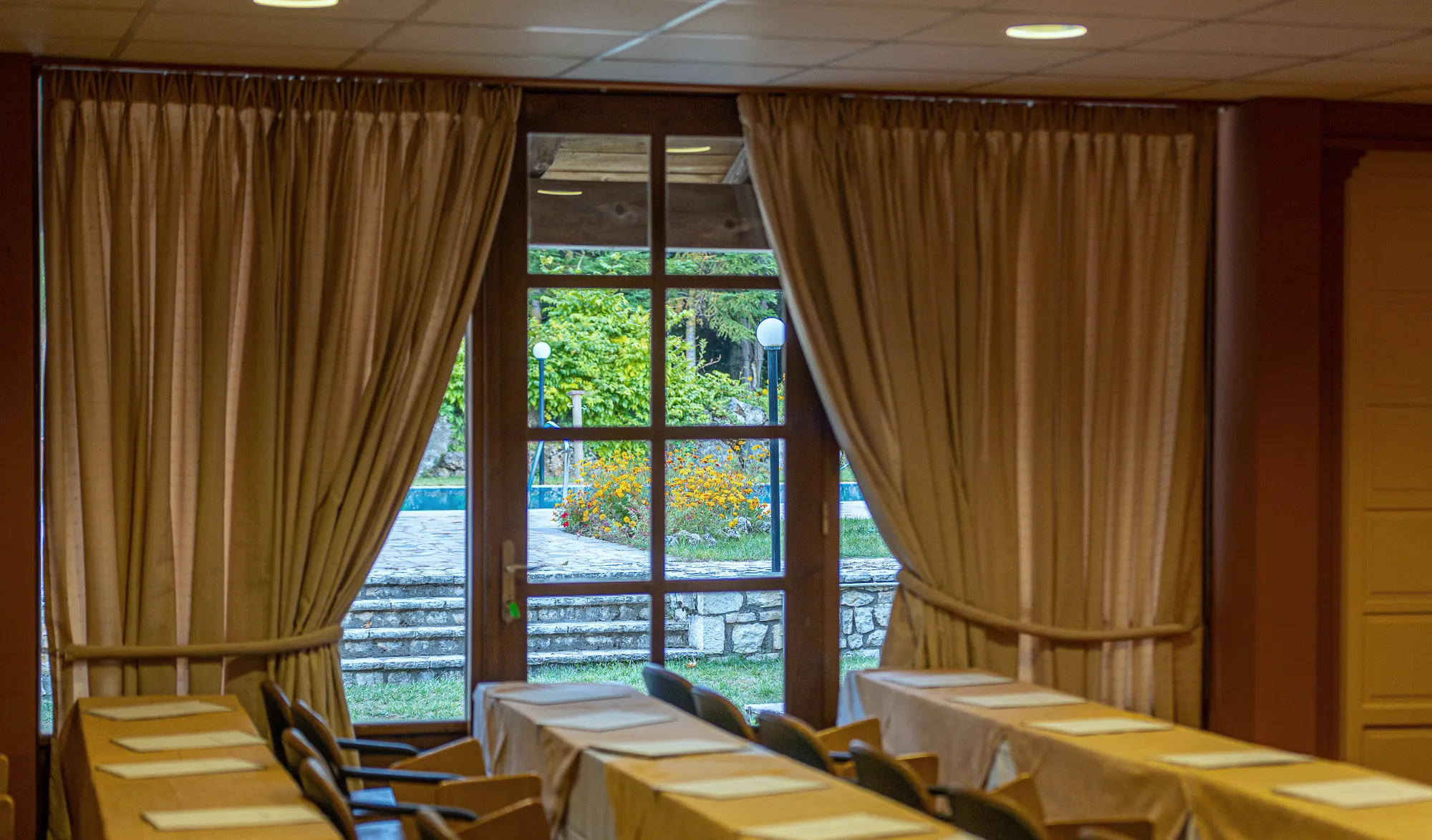 Tall windows with curtains in the conference room, looking onto the garden and a stone stairway