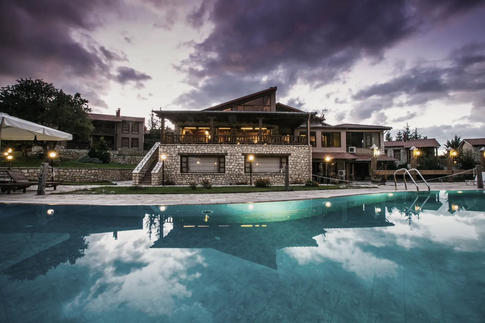 Η πισίνα και το κεντρικό κτίριο του Vitina House στο σούρουπο
