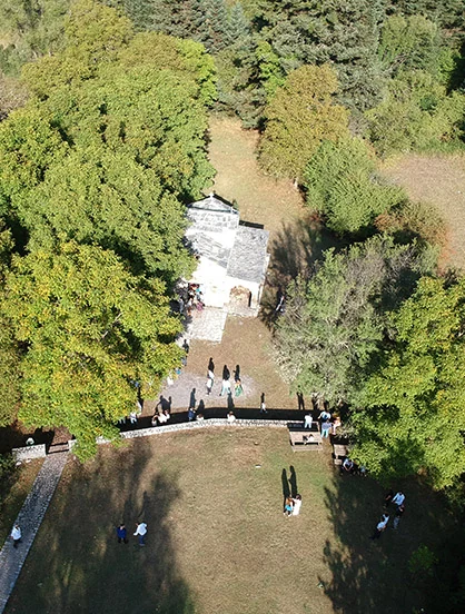 Aerial view of a small stone chapel among trees, with guests gathered on the grass