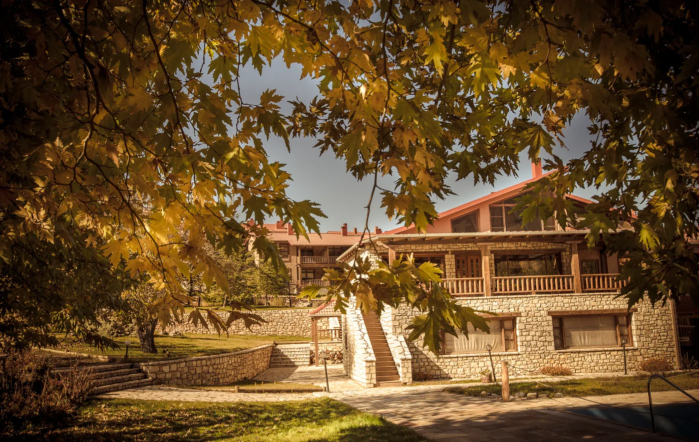 Gardens of Vitina House in autumn, with coloured foliage and the stone buildings beyond