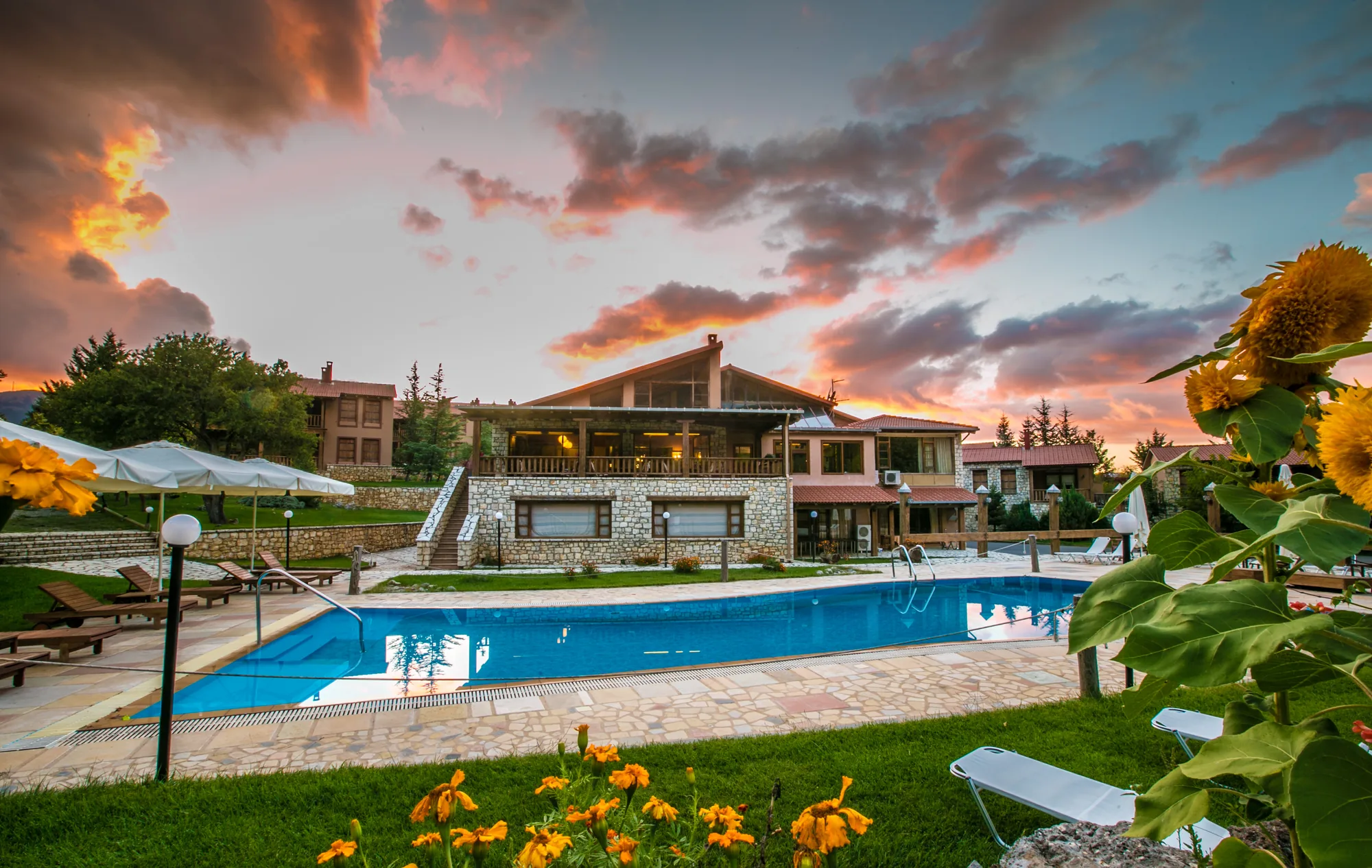 The pool and buildings of Vitina House at sunset, with the forested slopes of Menalo behind