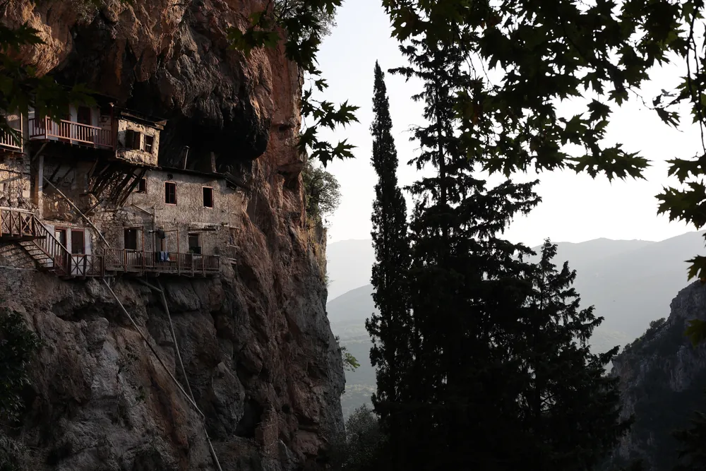 Wooden balconies of a monastery built into a cliff, with cypress trees in front