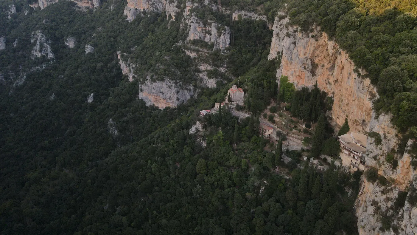 Aerial view of a monastery on the orange cliff of a wooded gorge