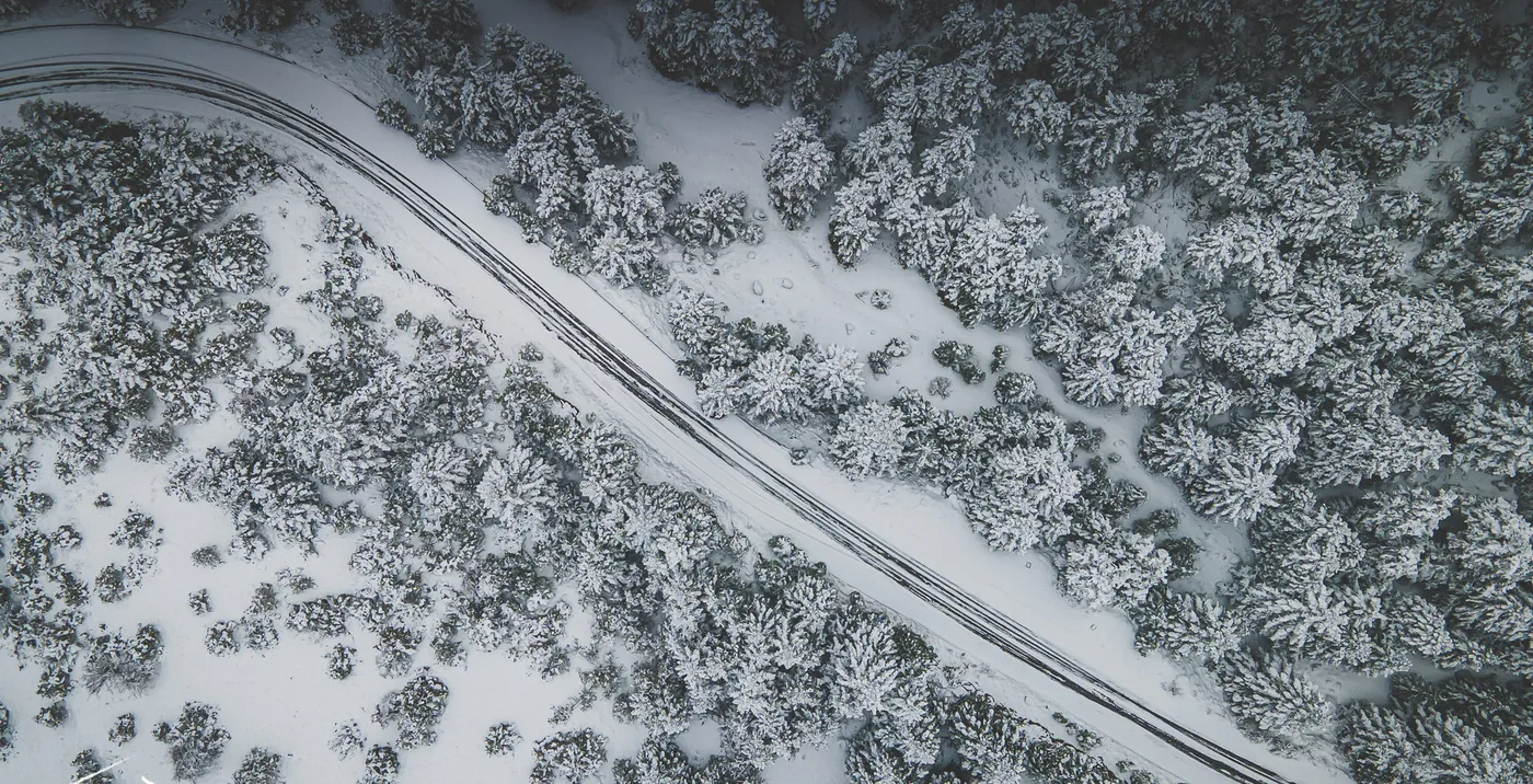 Aerial view of a road curving through snow-covered firs on Menalo