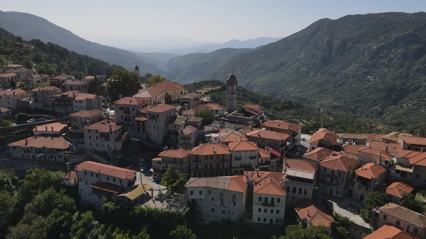Aerial view of a stone village with red tiled roofs and a bell tower above a forested valley