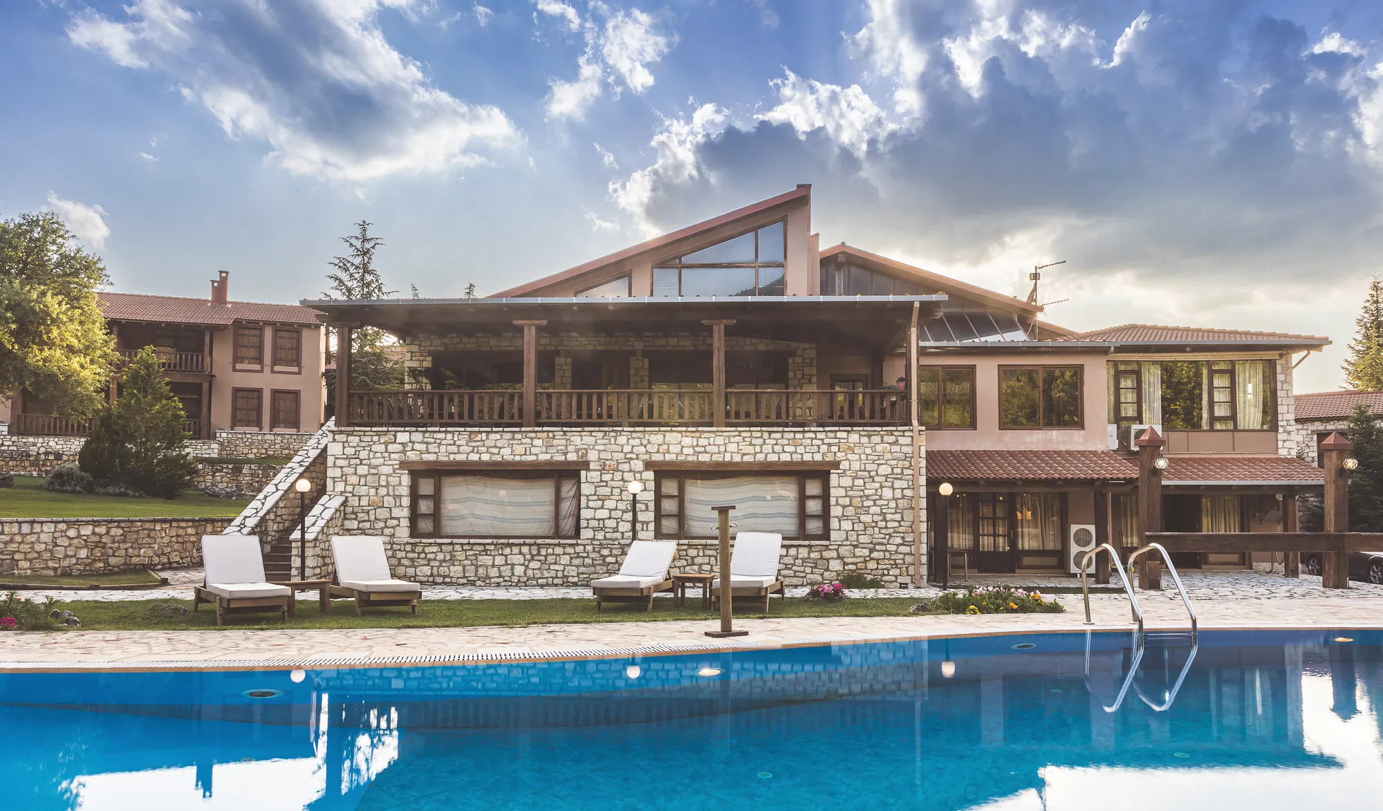 Το κεντρικό κτίριο και η πισίνα σε φωτεινή μέρα, με σύννεφα πάνω από τη στέγη
