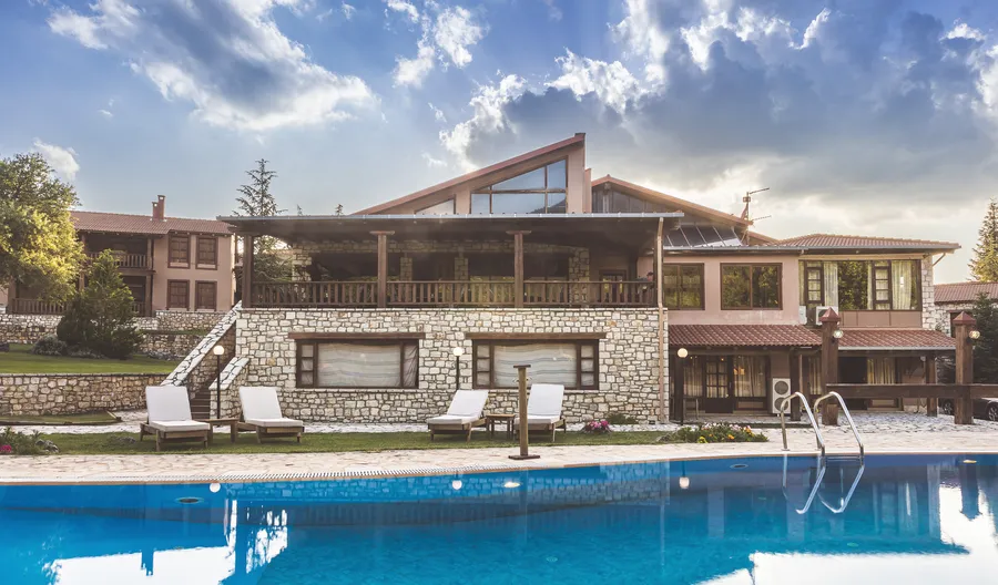 Το κεντρικό κτίριο και η πισίνα σε φωτεινή μέρα, με σύννεφα πάνω από τη στέγη