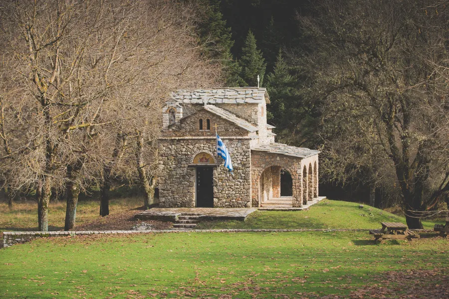 A small stone chapel in a grassy clearing, with a flag