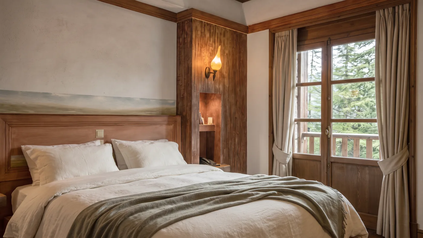Close view of the Premium room bed with white pillows, a grey throw and the balcony door