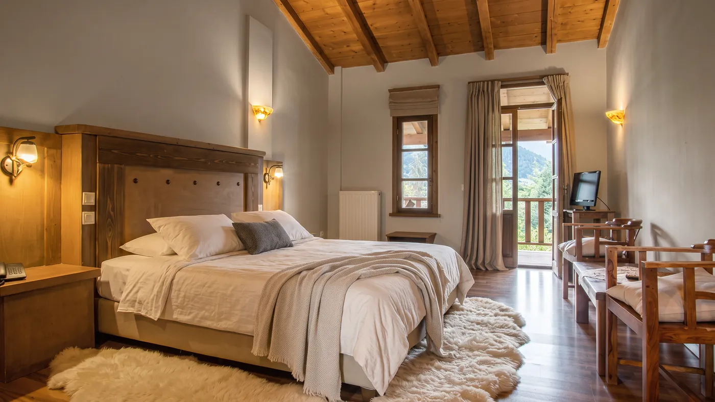 Standard room with a timber ceiling, linen bed and balcony door opening to the mountains