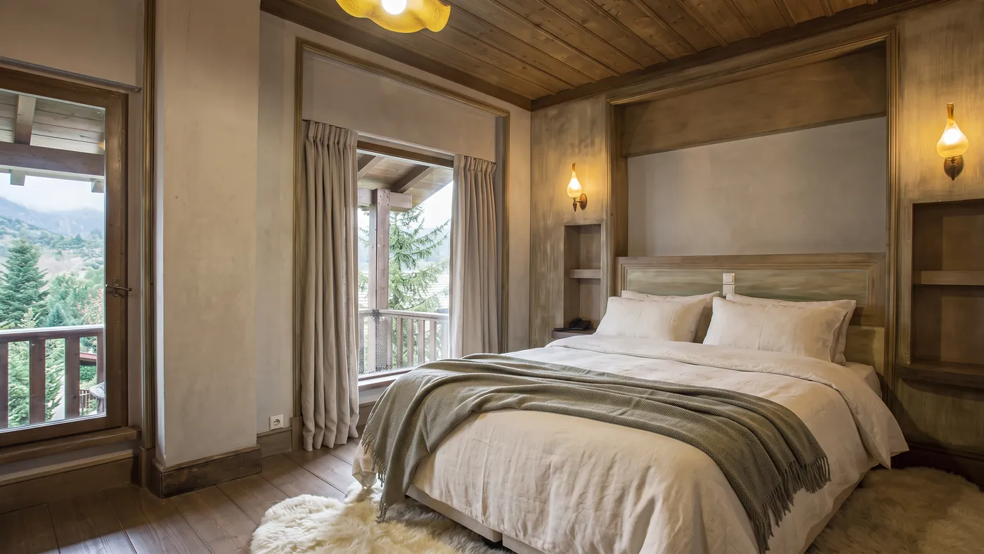 Suite bedroom with a timber ceiling, linen bed and a balcony looking onto the pines
