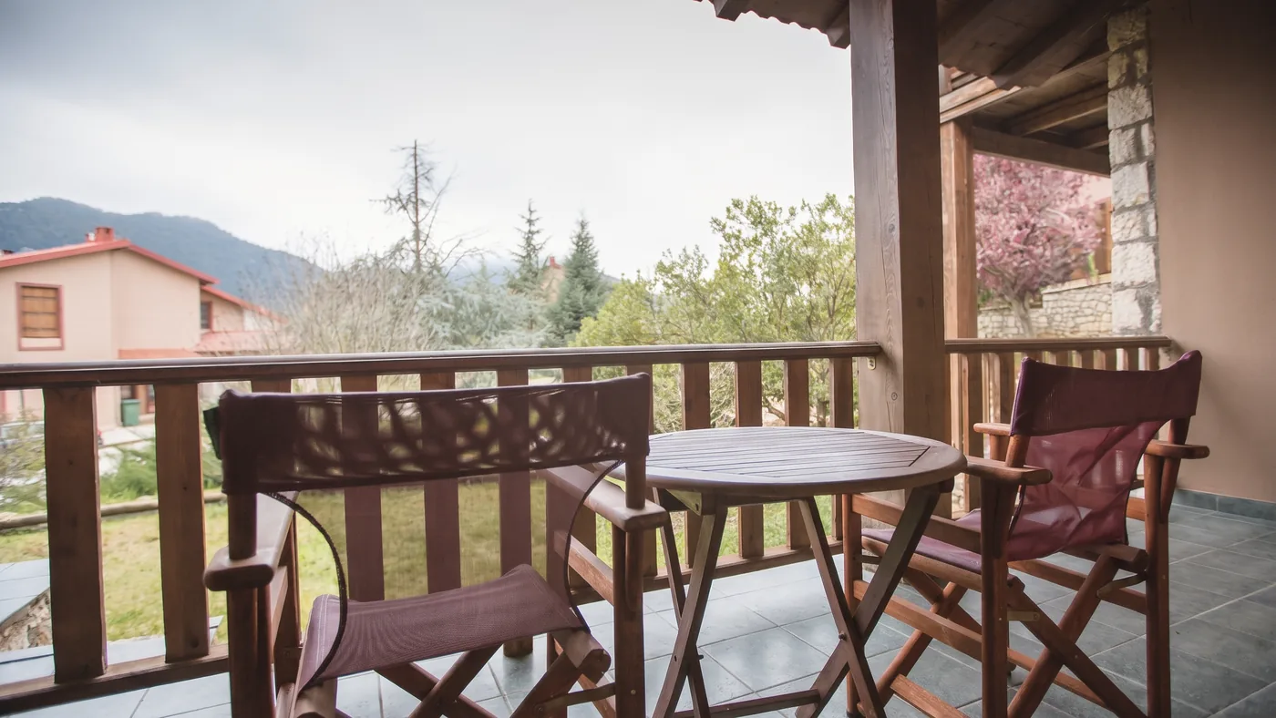 Balcony of the Standard room with wooden railings, a table and two chairs, and a view of the mountain and village