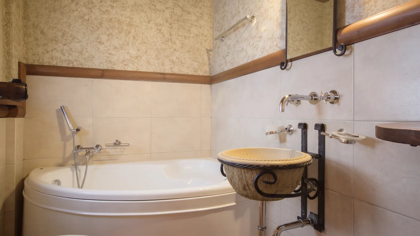 Bathroom with a corner bathtub, stone basin on an iron stand and tiled walls