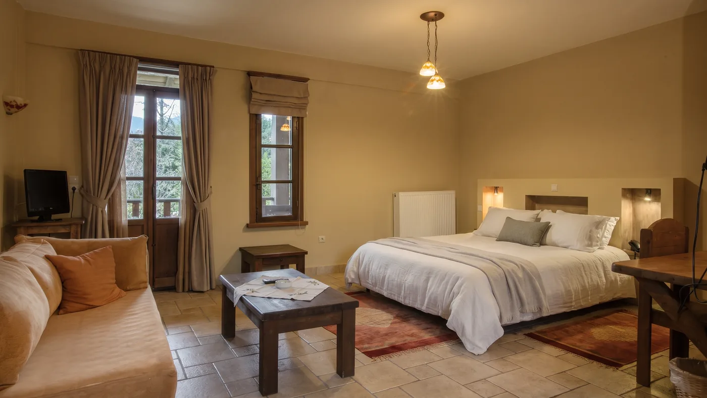 Standard room with a sofa, low table and bed on a tiled floor, with a balcony door and window