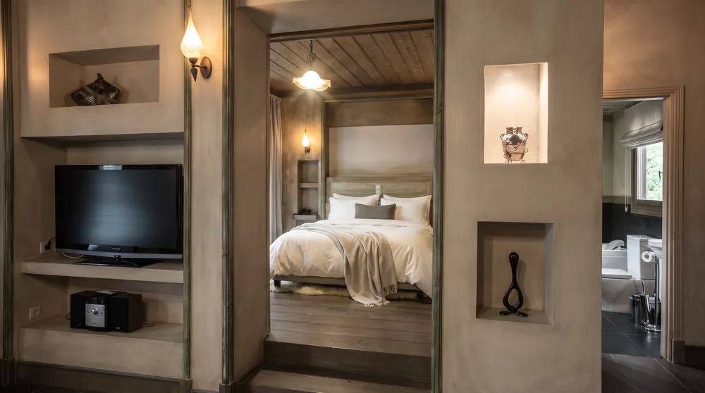 View through an arched opening from the living room to the bedroom, with a TV in a wall niche and the bed beyond