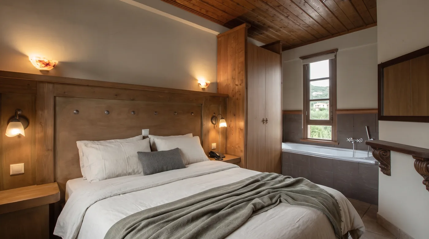 Double bed with white pillows and a grey throw in front of a timber headboard with wall lamps