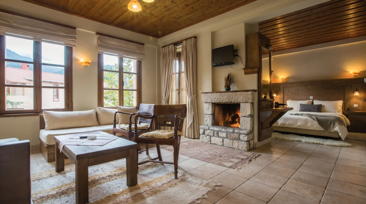 Superior room living area with a sofa, armchairs and a low table facing a stone fireplace, with the bed alcove beyond