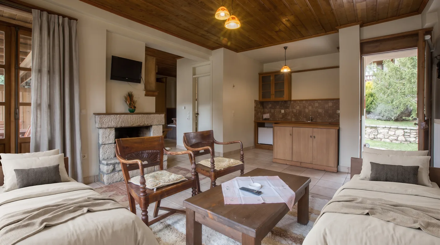 Living area of the Superior room with wooden armchairs, a low table, two day beds, the kitchenette and an open door to the garden