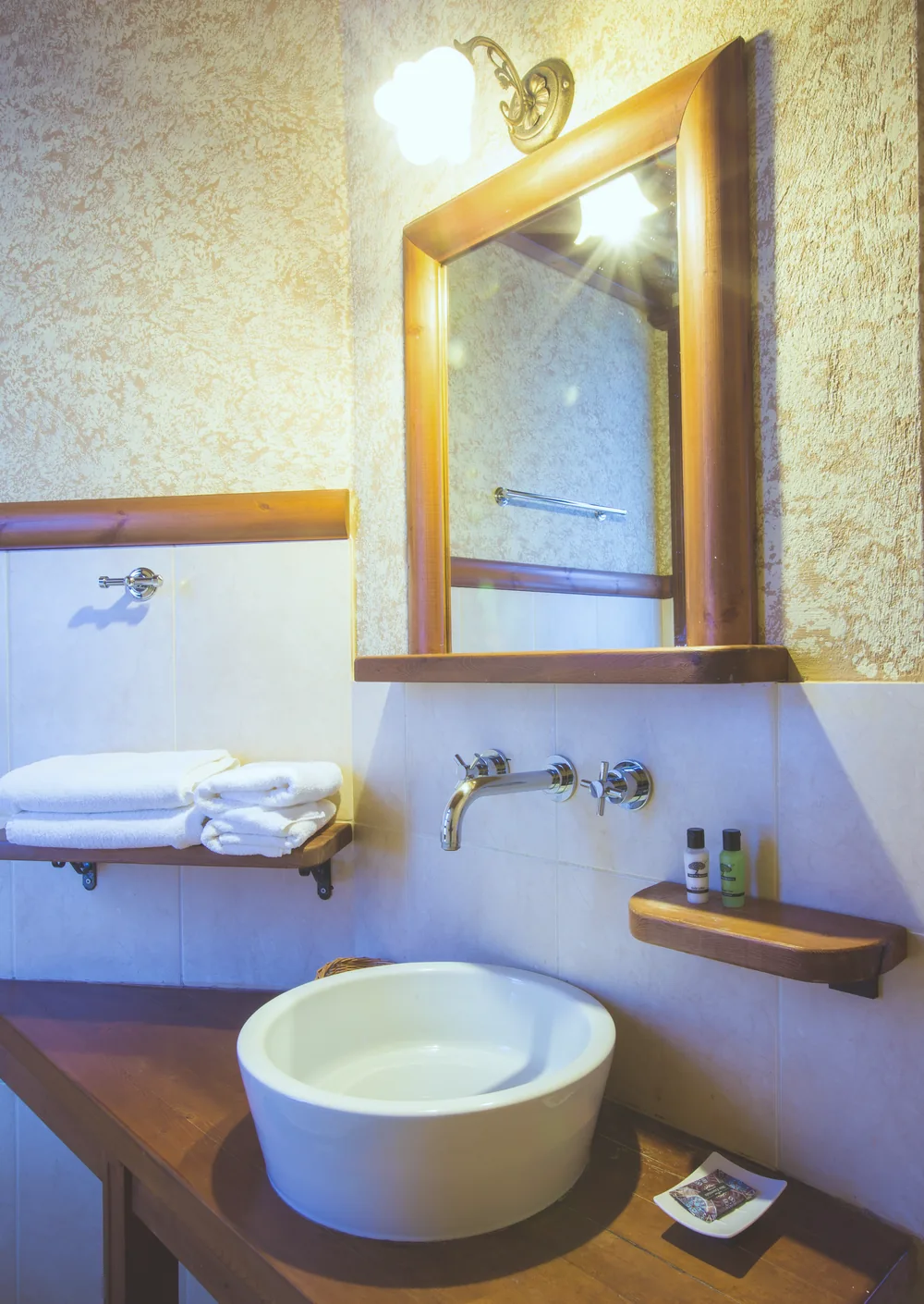 Bathroom with a round white basin on a wooden counter, a wood-framed mirror and towels