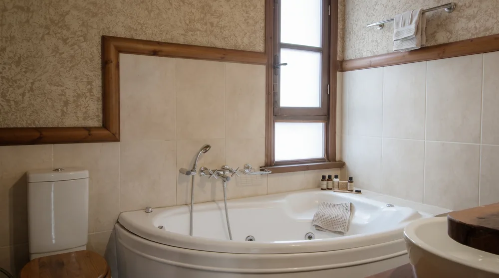 Bathroom with a white corner whirlpool bath, a small window and wood-framed tiling