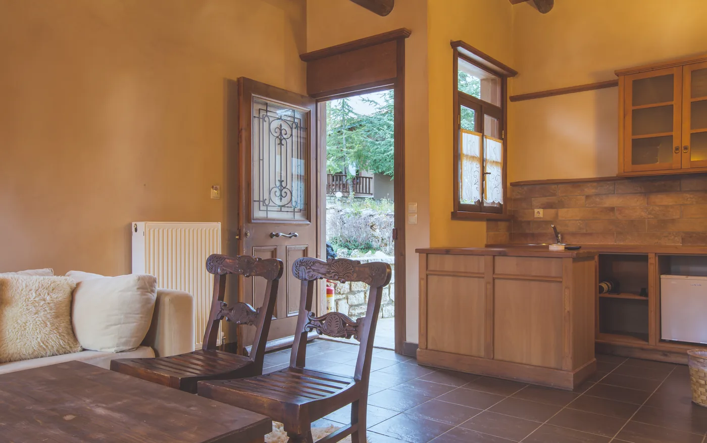 Villa interior with a wooden front door open onto the garden, a sofa with sheepskin cushions and a wooden cabinet